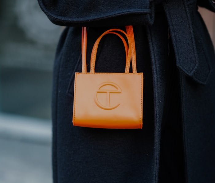 NEW YORK, NEW YORK - FEBRUARY 12: A guest wears a black belted long winter coat, an orange shiny lea...
