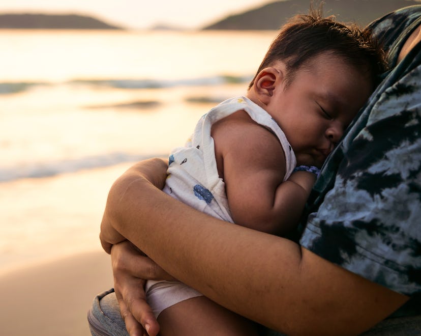 baby burying face in parent's chest on beach
