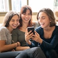 Brazilian family sitting on sofa, looking at social media on smartphone, smiling and laughing