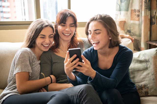 Brazilian family sitting on sofa, looking at social media on smartphone, smiling and laughing