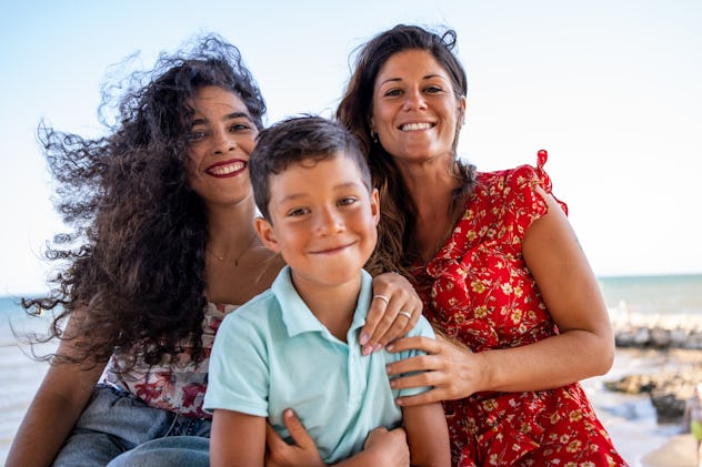Portrait of two women embracing a young boy on a sunny beach.
