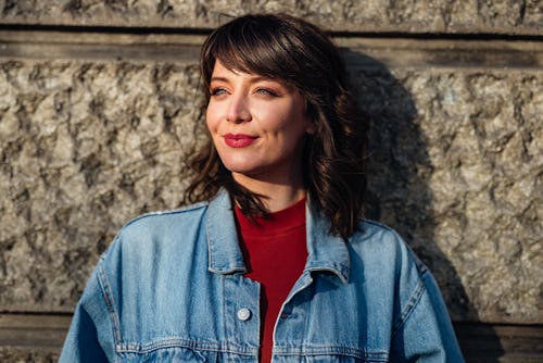 Cropped photo of a woman in denim jacket leaning against a stone wall. Here's everything you need to...