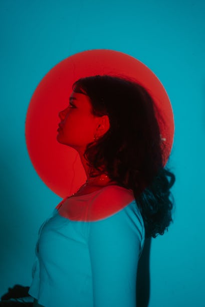 Young woman posing under a bright red light during Mercury retrograde spring 2022, which will affect...