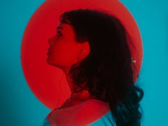 Young woman posing under a bright red light during Mercury retrograde spring 2022, which will affect...