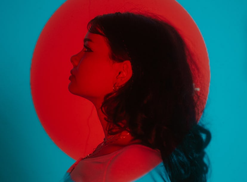 Young woman posing under a bright red light during Mercury retrograde spring 2022, which will affect...