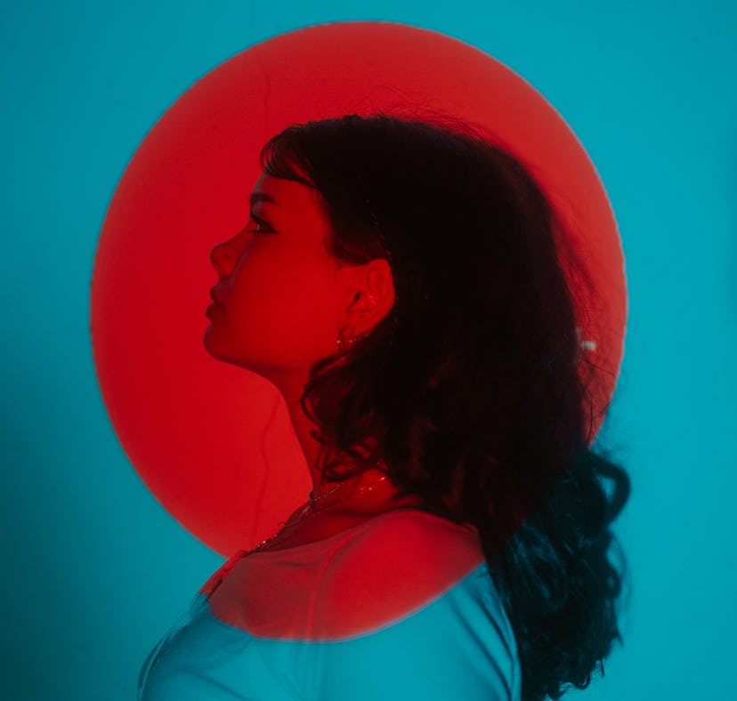 Young woman posing under a bright red light during Mercury retrograde spring 2022, which will affect...