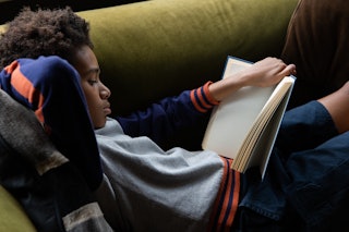 Portrait of 12 year old boy reading a book, at home on the sofa