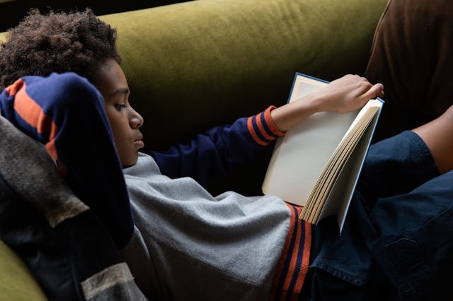 Portrait of 12 year old boy reading a book, at home on the sofa