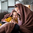 Tween sisters snuggled under blanket and watching a movie on digital tablet.