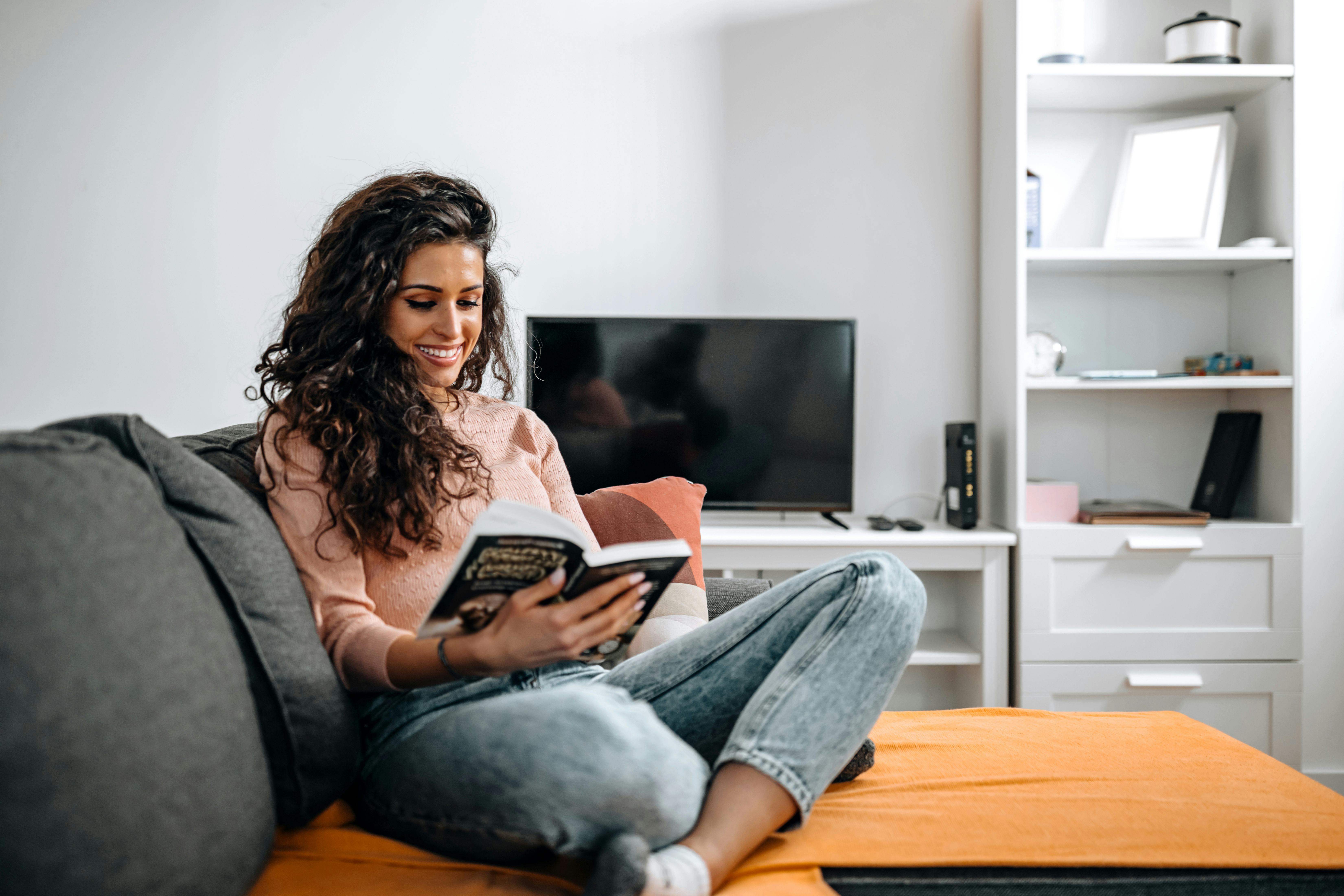 Beautiful young woman sitting in living room and reading a book on weekend.leisure, literature and p...