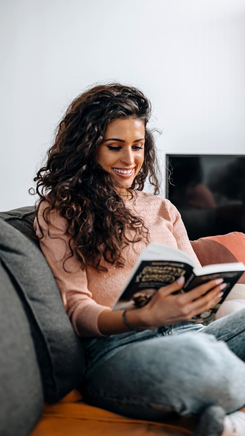 Beautiful young woman sitting in living room and reading a book on weekend.leisure, literature and p...