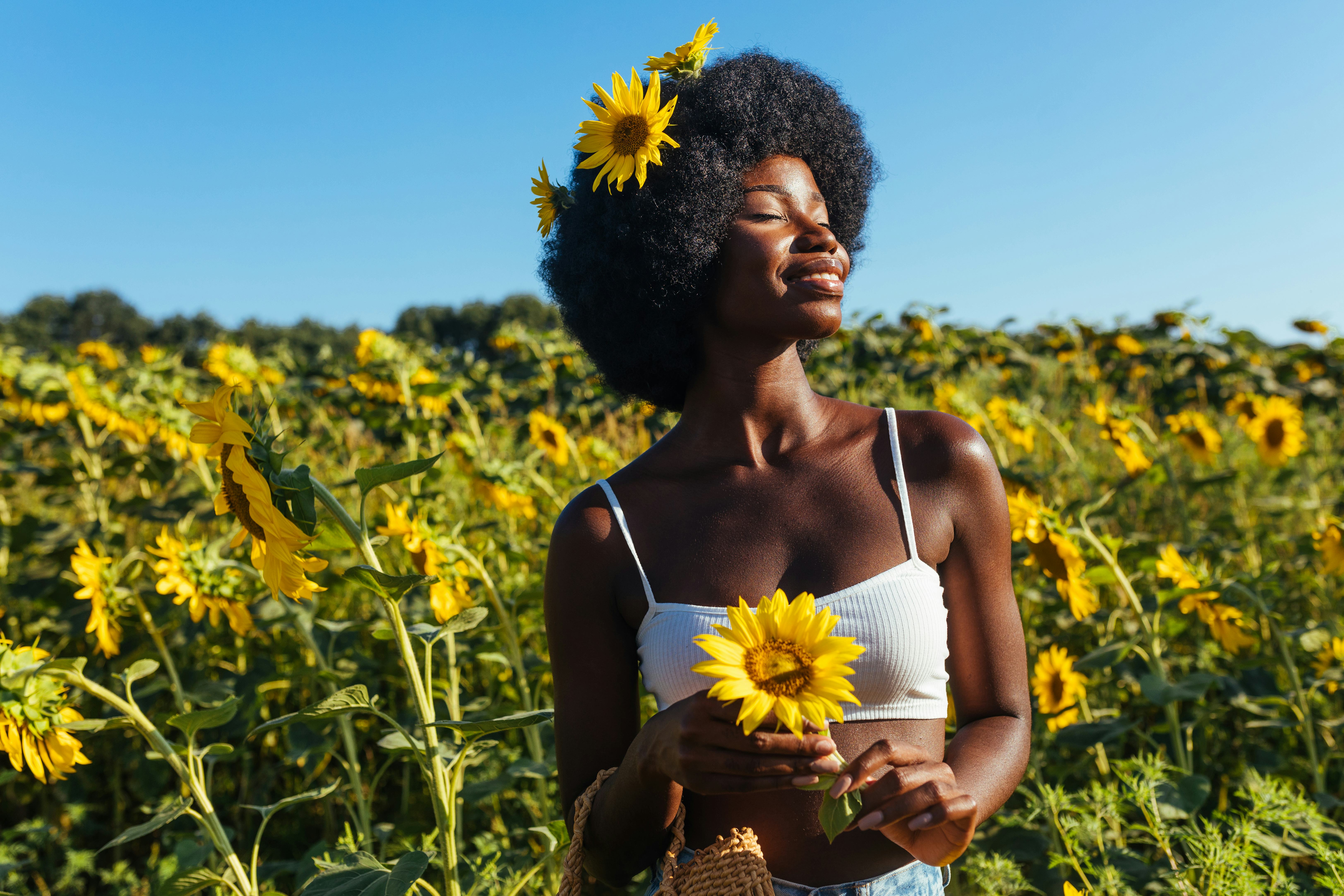 Woman with sunflowers in her hair smiling in a sunflower field. Taurus season 2022 begins April 19 a...