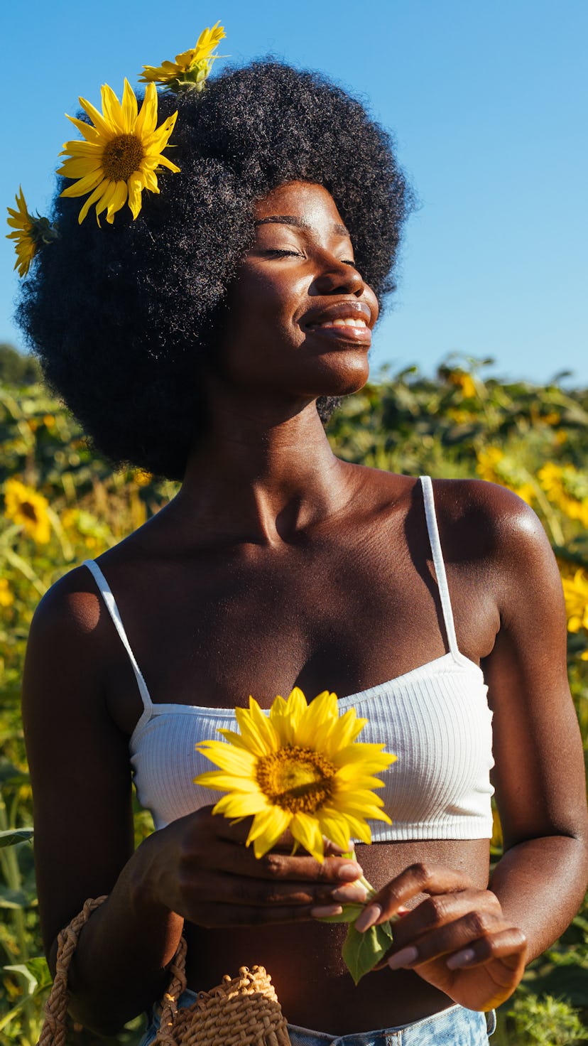 Woman with sunflowers in her hair smiling in a sunflower field. Taurus season 2022 begins April 19 a...