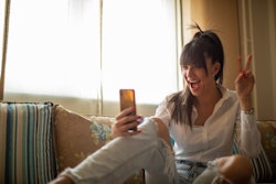 A woman flashes a peace sign while taking a selfie on the BeReal app. Here's how to use the BeReal A...