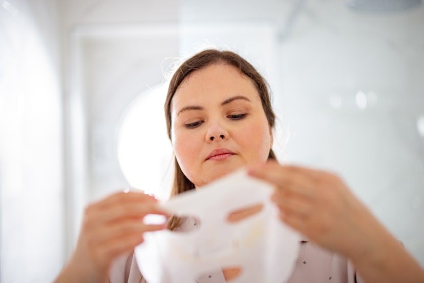 Portrait of a plus size woman holding a white face mask product and applying it to her face.