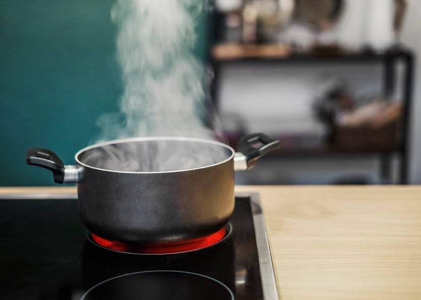 Dark cooking pot with water steam on stove with kitchen background. Cooking preparation at home. Fro...