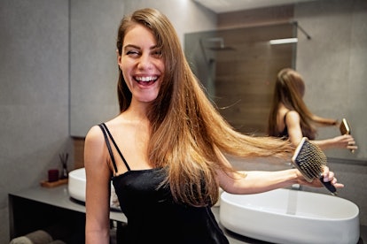 Portrait of young woman combing her hair in bathroom