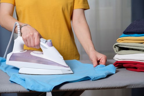 Lots of bright, clean, multicolored pressed clothes stacked on the ironing board. A woman or a girl,...