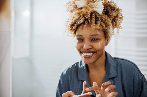 Beautiful happy woman applying face cream around her eye for her morning beauty routine in her bathr...