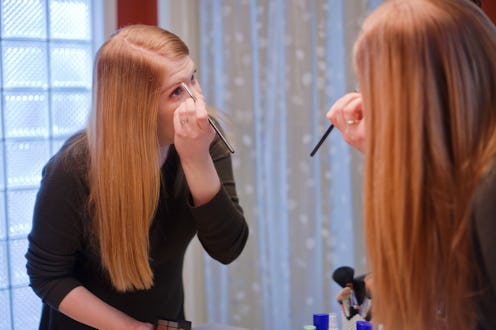 A young woman applies make-up in her bathroom.