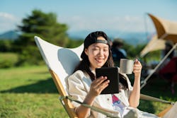 A woman reads the morning newspaper at a campground. Here's your April 19 zodiac sign daily horoscop...