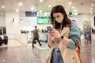 Portrait of a beautiful young woman on vacation arriving on the airport and using smartphone