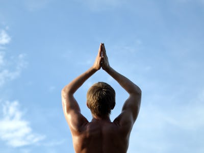 guy does yoga and stands in a meditative pose against a blue cloud sky