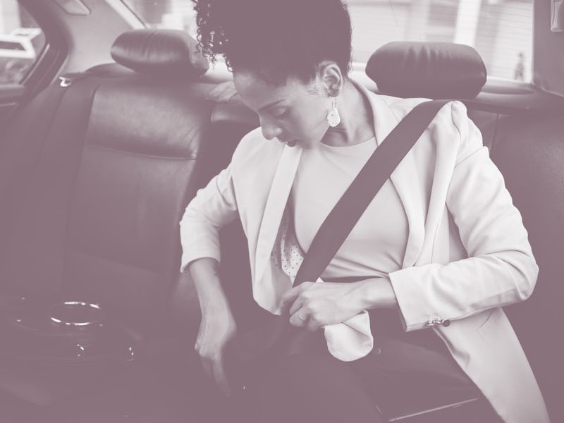 Young businesswoman putting on a seat belt before riding in the back seat of a taxi during a busines...