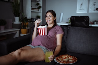 A pregnant woman eats popcorn while she watches a movie.