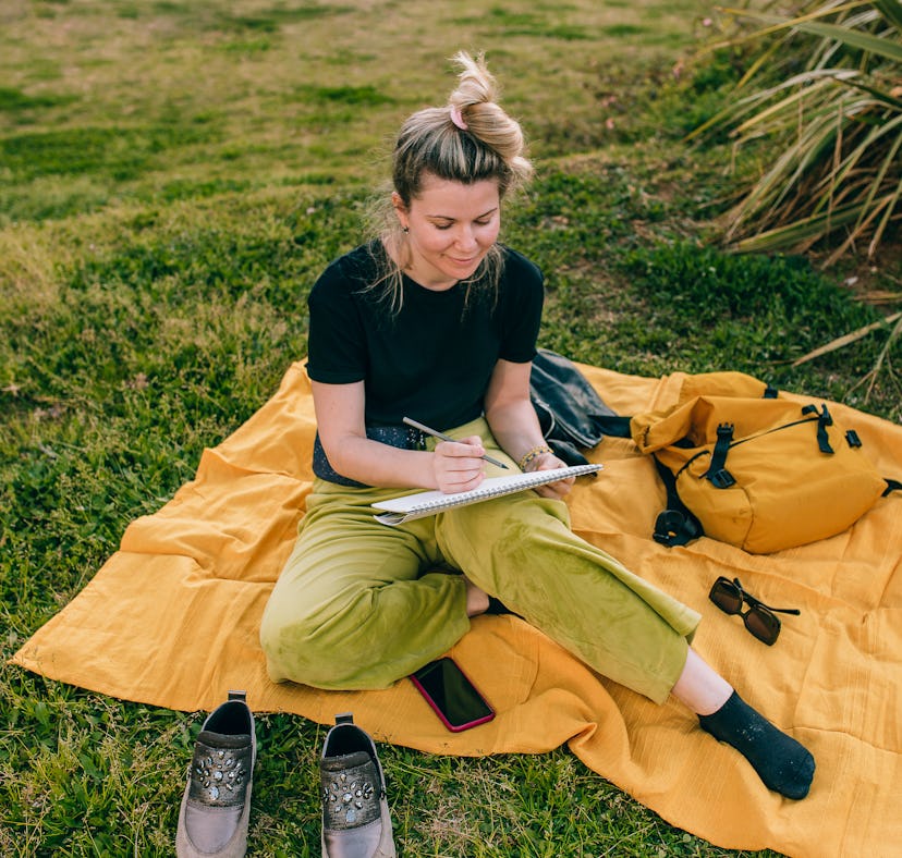 A woman sketches while on a picnic, which is one of the Earth Day activities on TikTok.