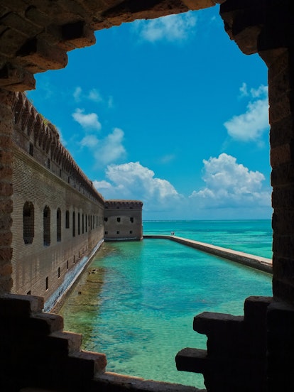 A view through a partial casemate wall of the fort with the salt water moat between the beach and fo...