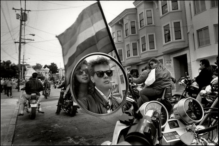 Their faces reflected in the motorcycle mirror under a Pride flag, a pair of women in the 'Dykes on ...