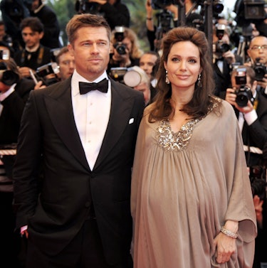 Brad Pitt in a suit and pregnant Angelina Jolie in a flowy dress with a bedazzled collar posing at t...