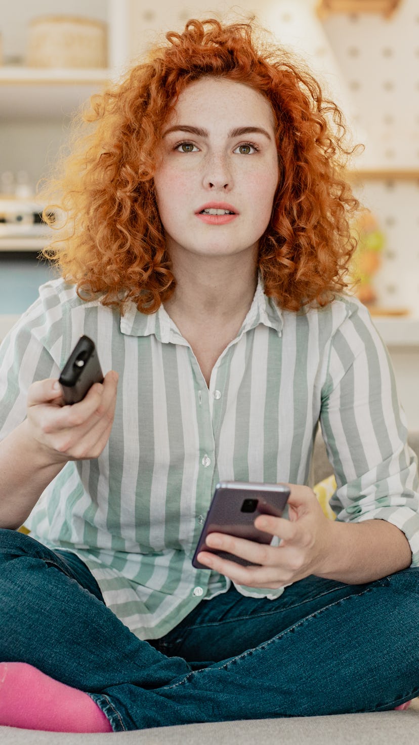 A young woman is watching tv at home. Netflix's password-sharing crackdown, explained.