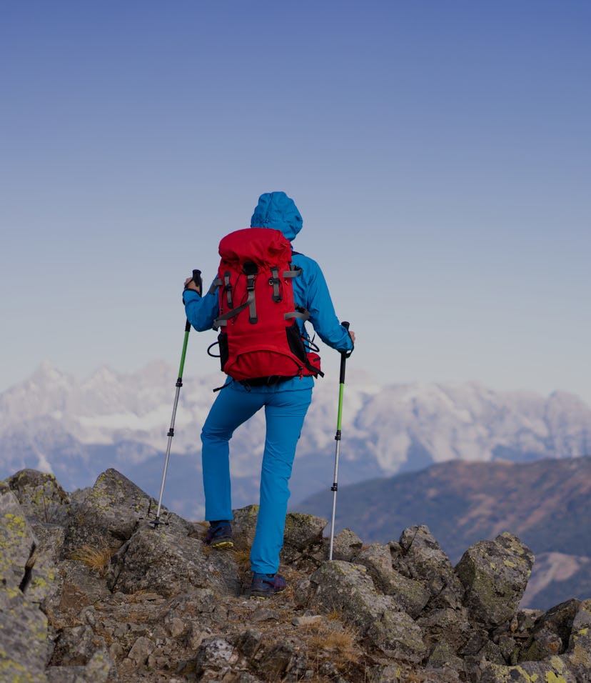 Rear view mountaineer hiking woman with backpack and hiking poles standing alone on mountain top on ...