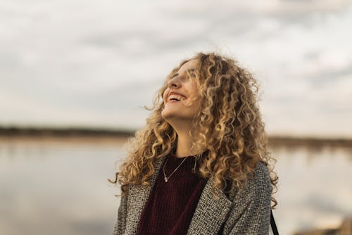 Happy blonde curly beautiful girl in coat against sky. The spiritual meaning of april's new moon sol...