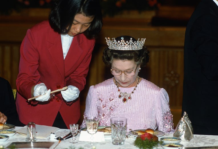 PEKING, CHINA - OCTOBER 13: Queen Elizabeth ll is offered chopsticks as she studies her food during...