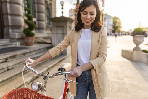 Smiling young woman walking and pushing her retro bicycle. These zodiac signs will be least affected...