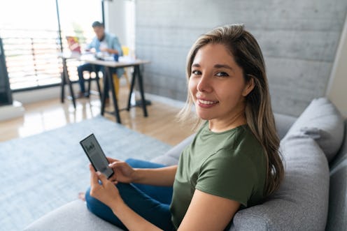 Happy woman texting on her cell phone while relaxing at home and with her husband working at home at...