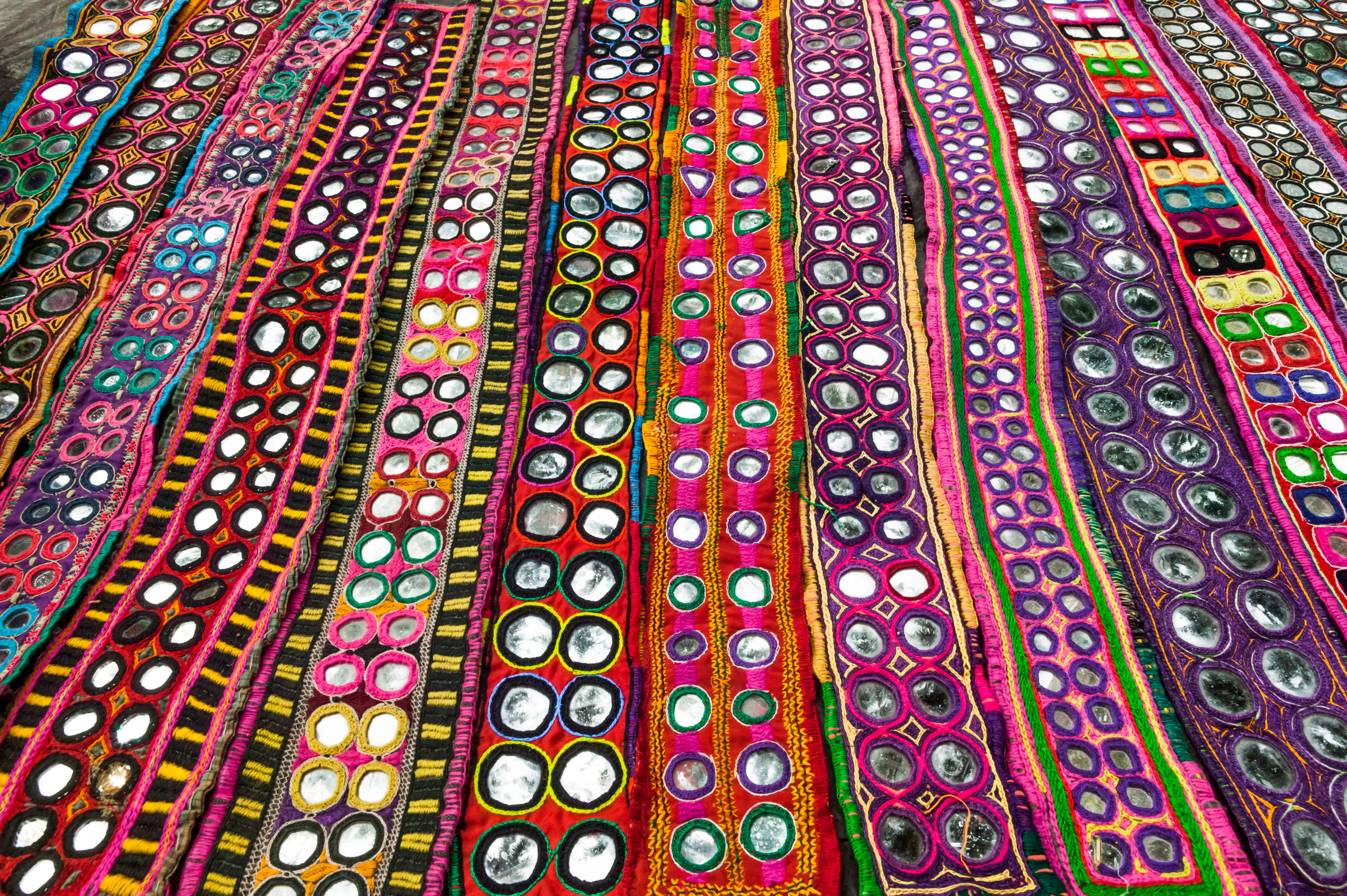 India, Goa, Anjuna Wednesday Market, display of colorful textiles with inlaid mirrors