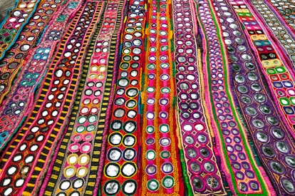 India, Goa, Anjuna Wednesday Market, display of colorful textiles with inlaid mirrors