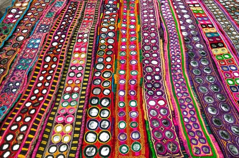 India, Goa, Anjuna Wednesday Market, display of colorful textiles with inlaid mirrors