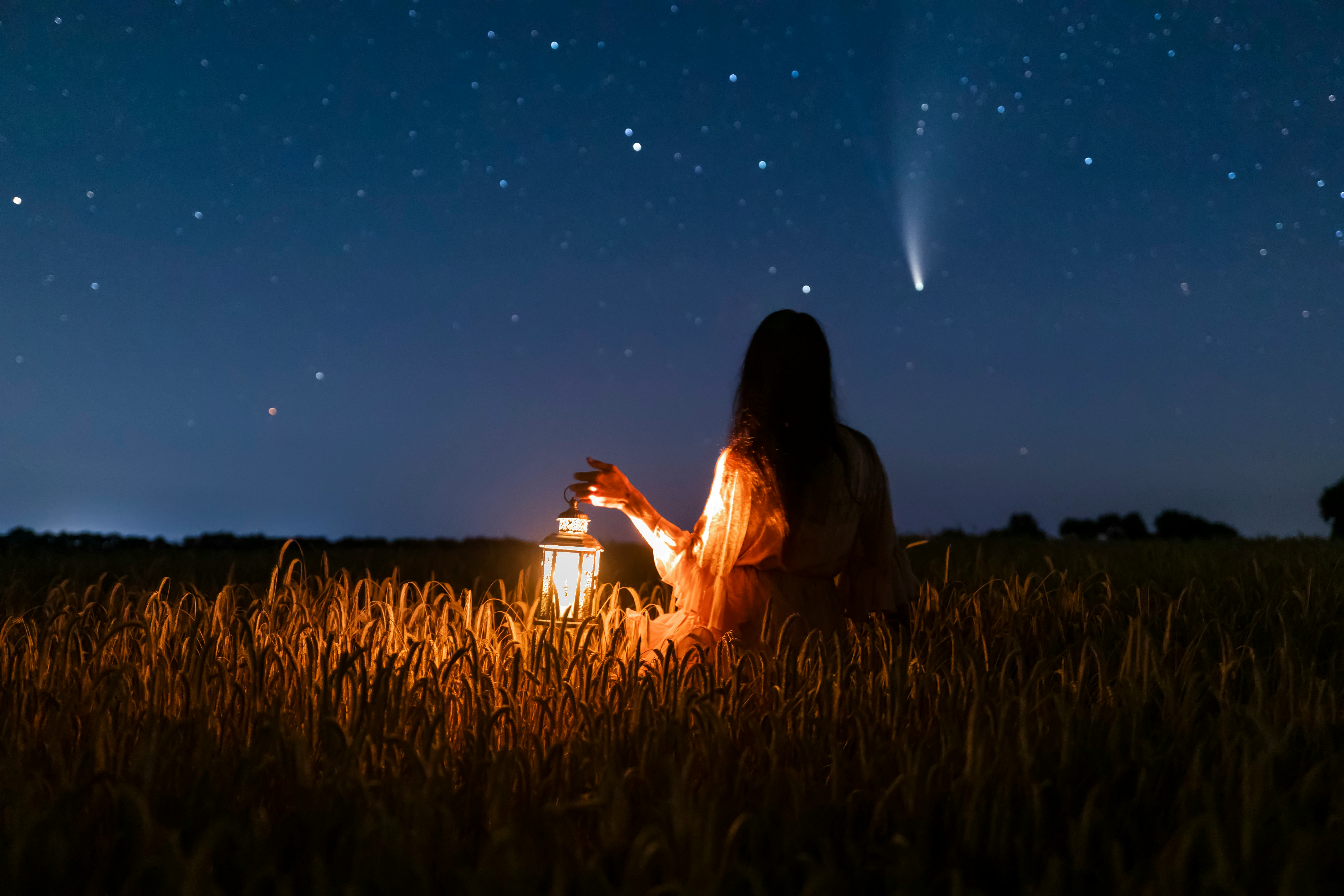A woman holding a lantern in the field while watching the night sky during April New Moon solar ecli...