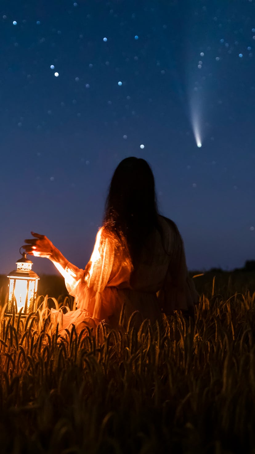 A woman holding a lantern in the field while watching the night sky during April New Moon solar ecli...