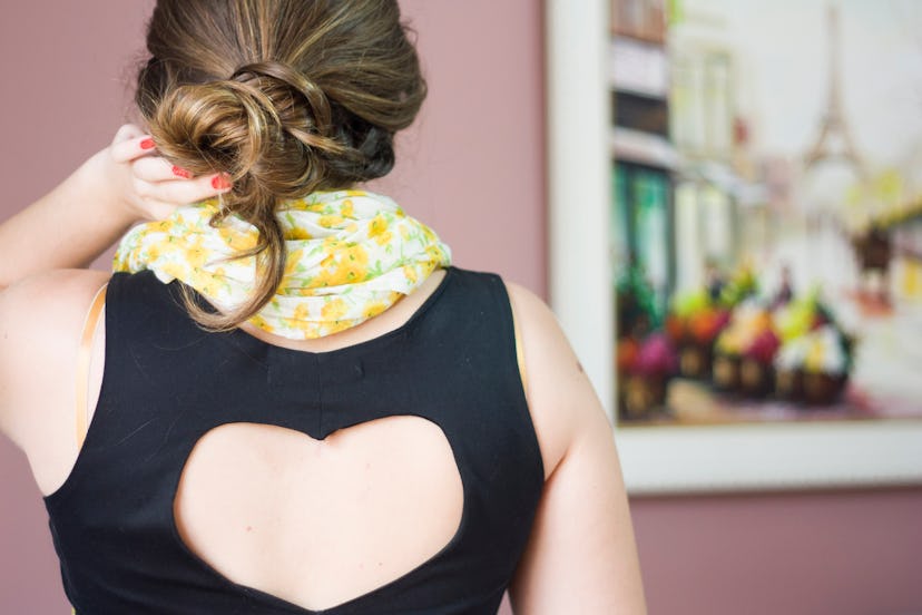 Girl with her hair in loose bun wearing yellow flowered scarf and black dress with heart on her back...
