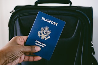 Close-up of unrecognizable black woman holding US passport next to packed suitcase