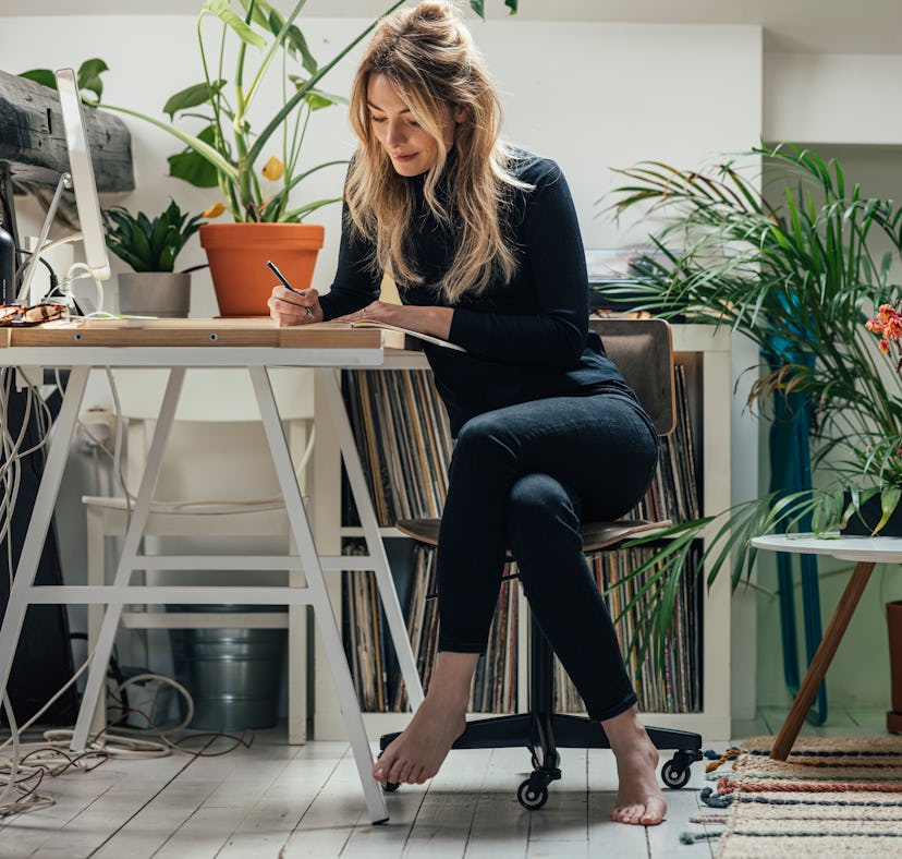 A charming Caucasian blonde smiling while writing her diary in the living room.