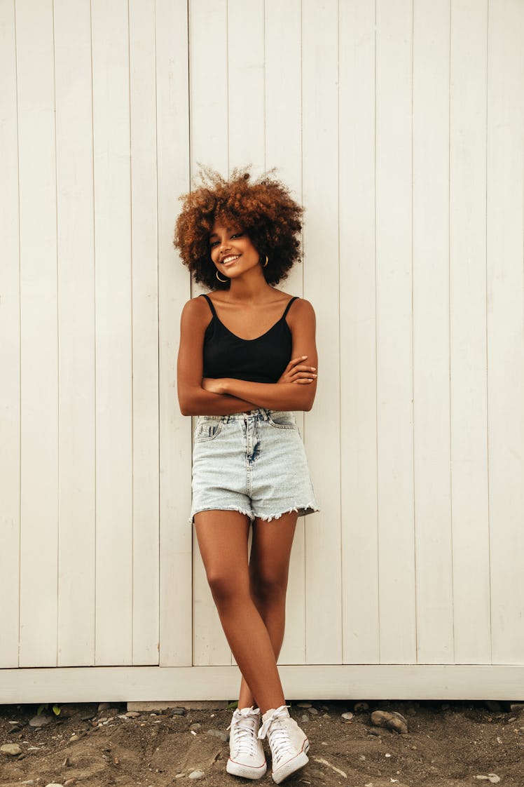 young woman leans against gate and smiles as she thinks about the 2022 Black Moon solar eclipse on A...