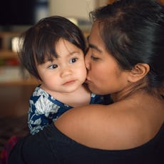 An Asian mother holding and kissing her mixed race toddler daughter.