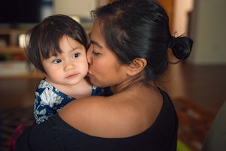 An Asian mother holding and kissing her mixed race toddler daughter.